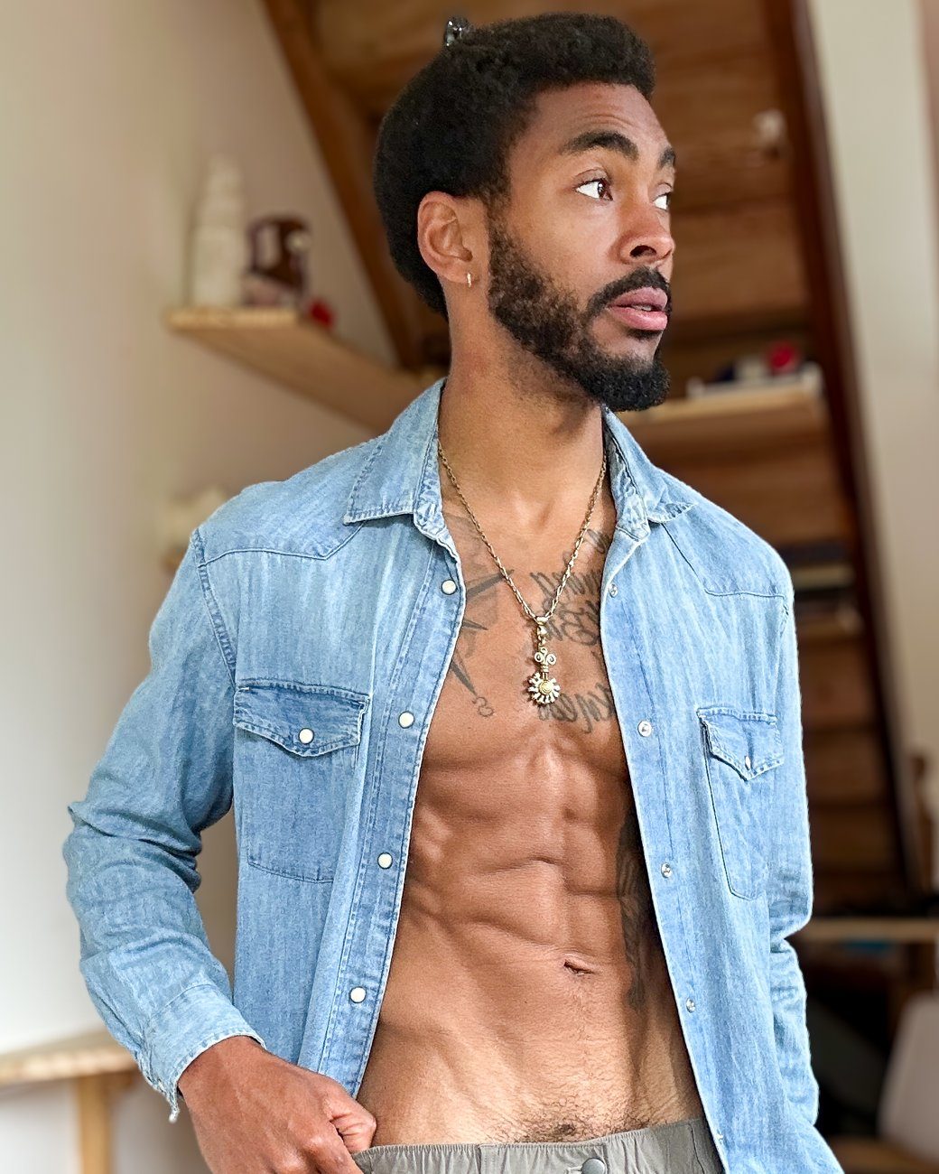 Zen at home in an open denim shirt, looking off to the side in the low warm light of a late evening.
